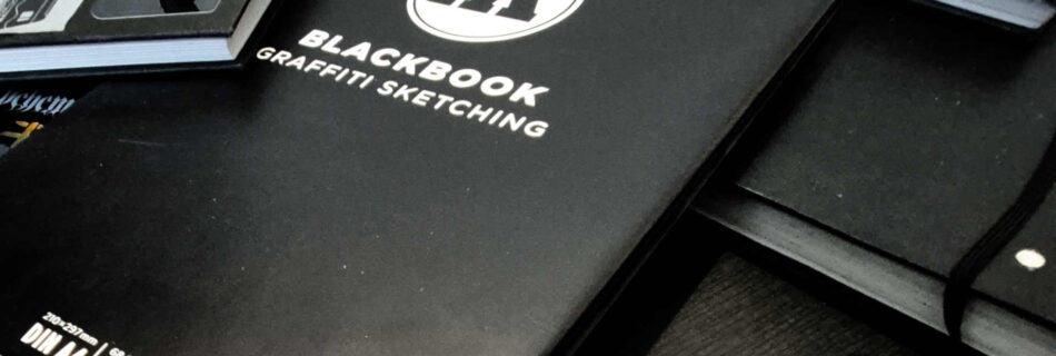 Many sketchbooks on top of each other, most of the books have stickers on their covers.