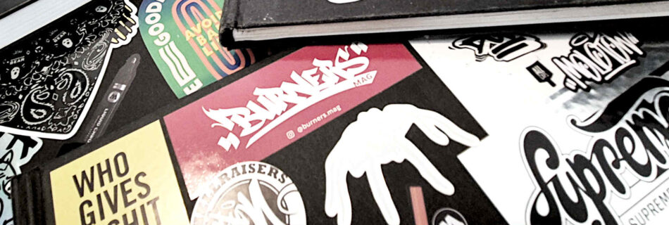 Many sketchbooks on top of each other, most of the books have stickers on their covers.