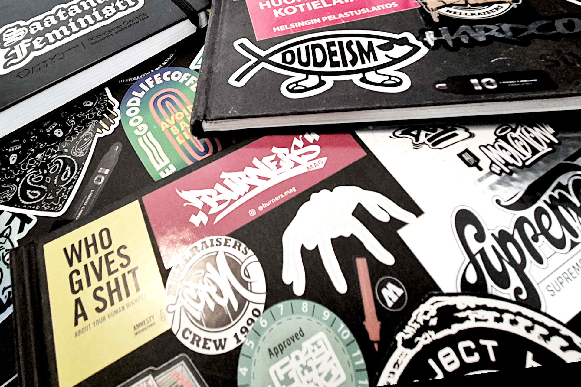 Many sketchbooks on top of each other, most of the books have stickers on their covers.