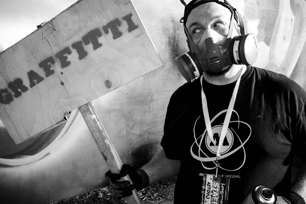 Person with a gasmask, holding a sign with mispelled text "graffitti".